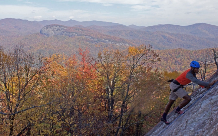 a person climbs a rock wall with fall foliage and a mountain landscape in the background